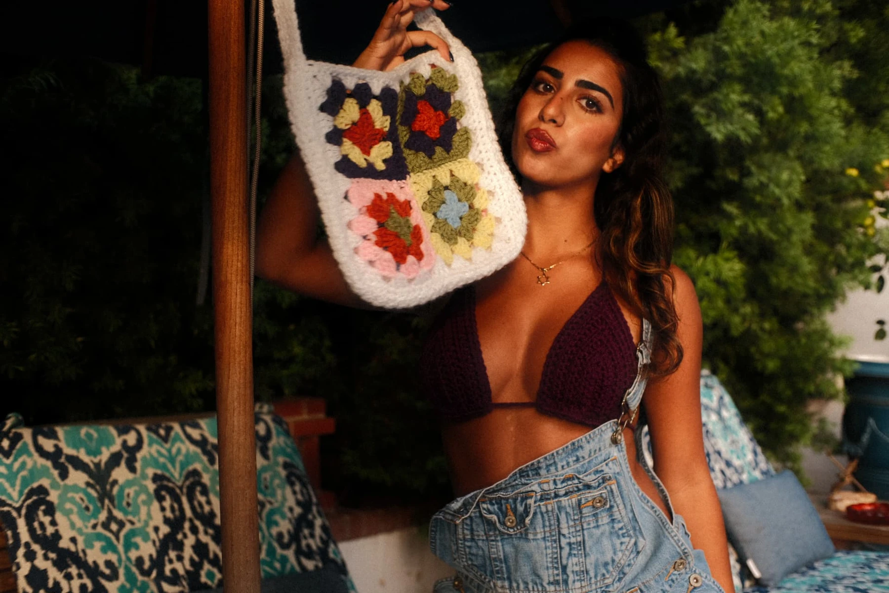 Floral crochet bag held up in a garden, styled with a purple crochet top and denim